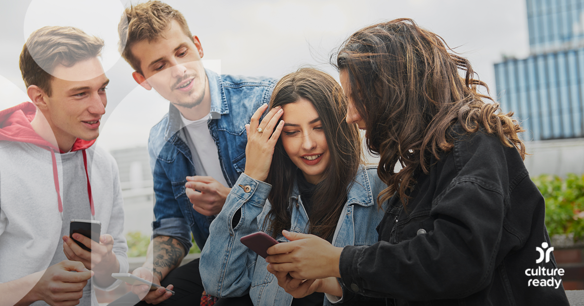 Two teenage boys and two teenage girls are wearing casual clothes and looking at their cell phones together