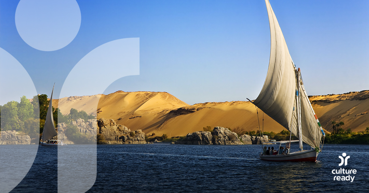 Two sailboats in on dark blue water in front of large sand dunes