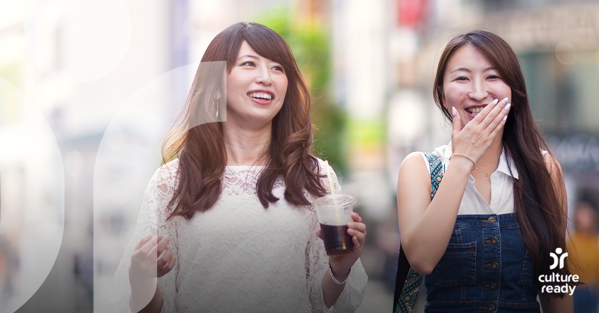 Two women dressed in casual clothes with dark brown hair are walking and having an animated conversation