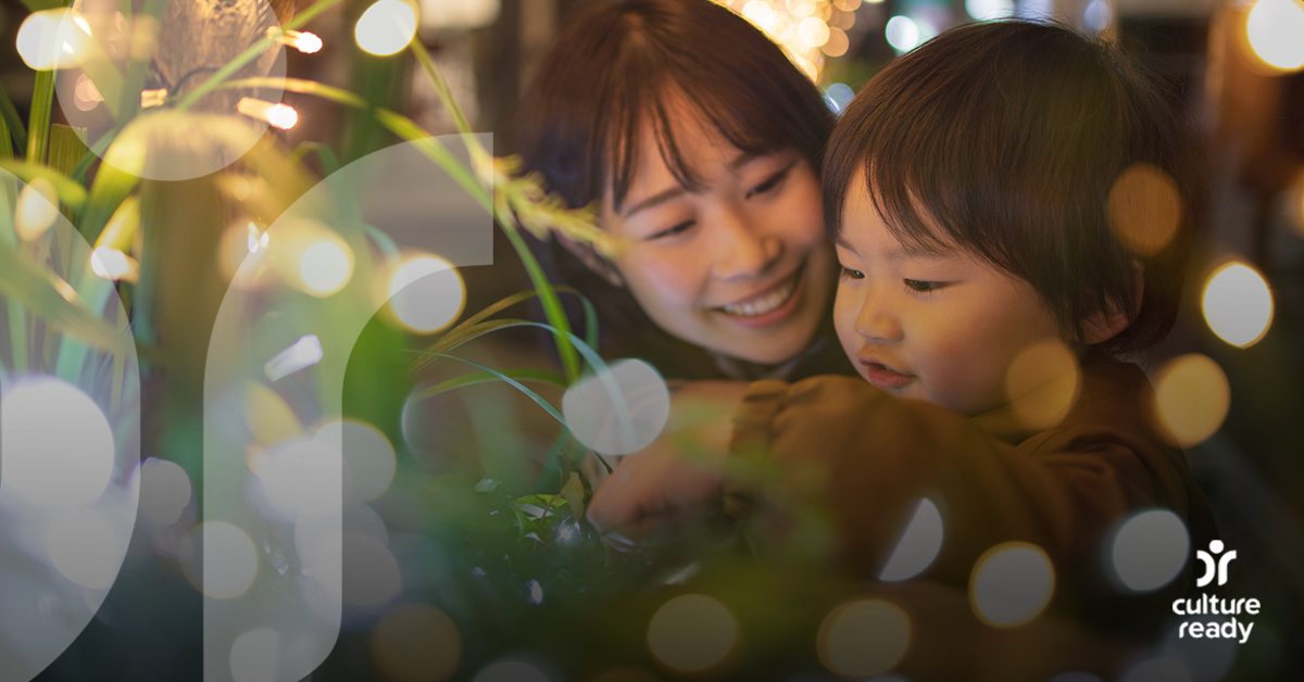 A close up of a woman and child with dark hair looking at lights on a Christmas tree