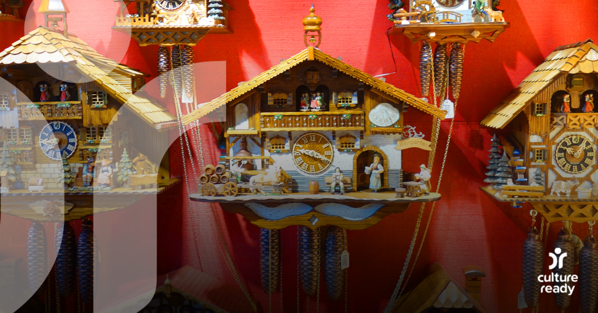 Five intricate, wooden German clocks are hanging up against a red wall