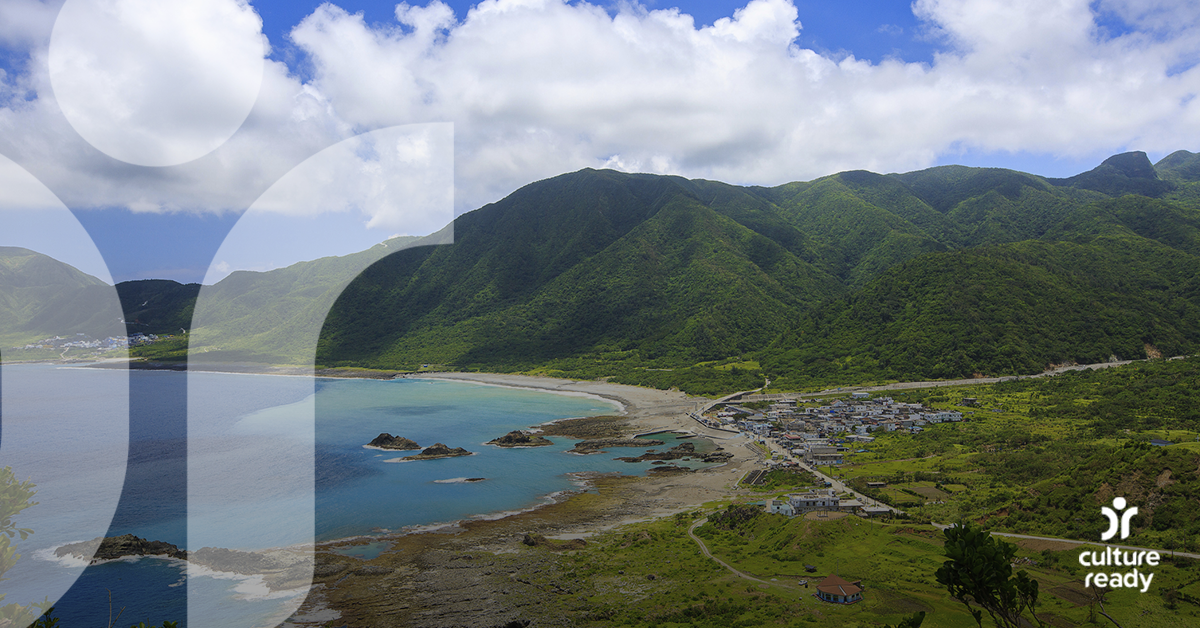A view of Orchid Island showing green hills, a bright blue bay, the Tao city and blue sky