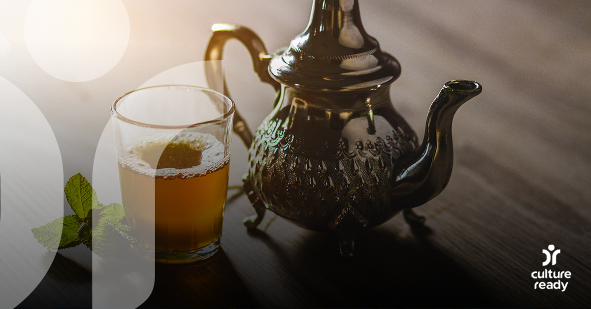 A metal tea kettle, next to a small glass of green tea with a sprig of mint