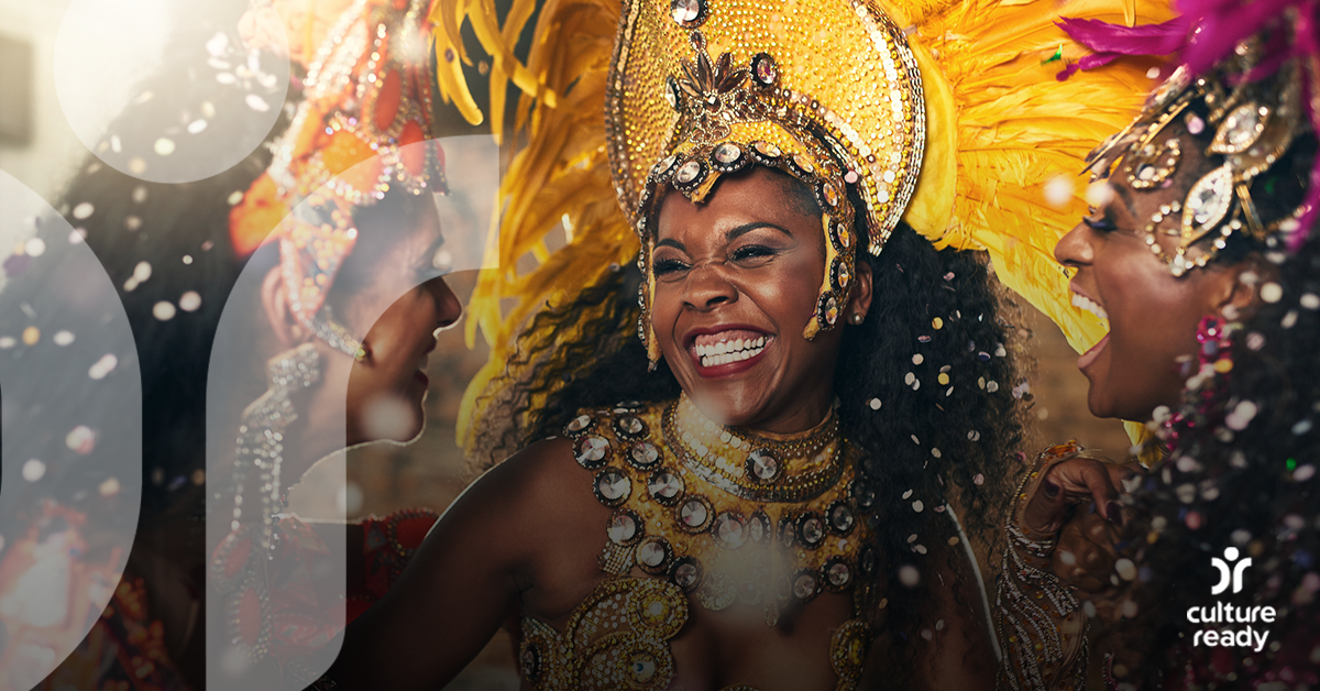 Three women wearing brightly colored Carnival costumes in yellow and purple laugh together