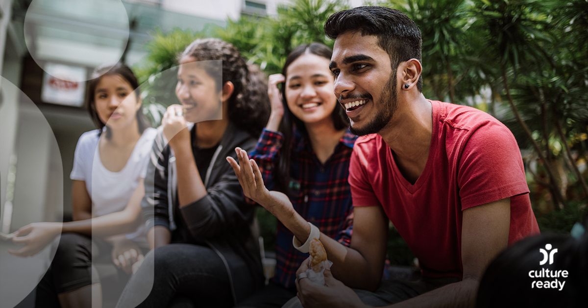 A group of four teenagers are talking and laughing outside in front of trees
