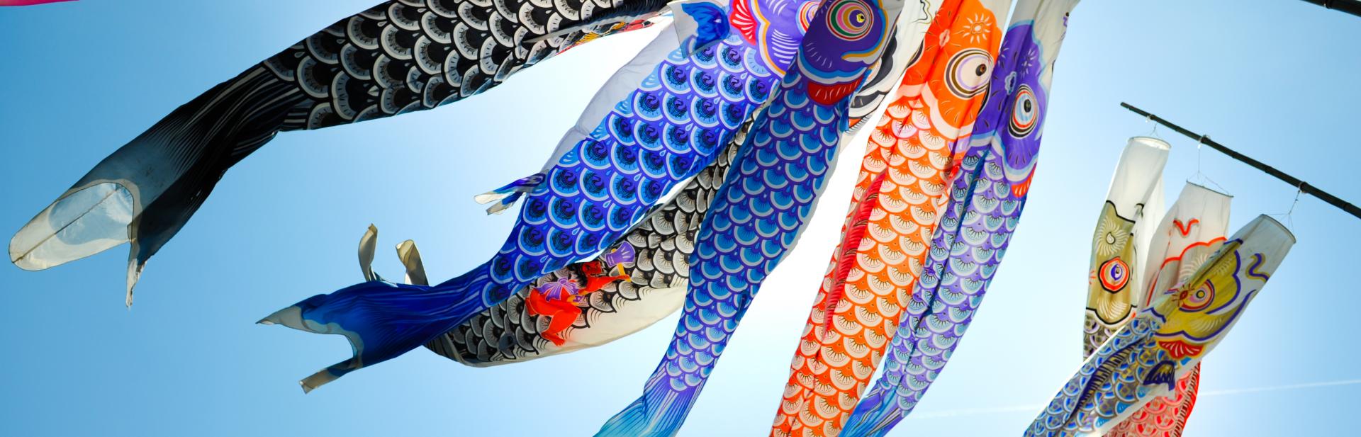 Fish kites blowing in wind against blue sky.