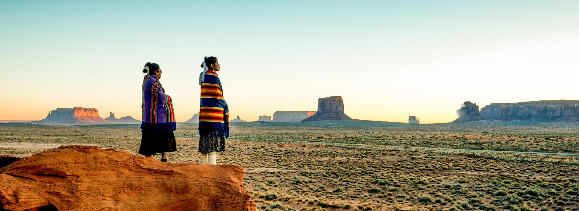 Women in traditional dress standing on cliff overlooking grasslands.