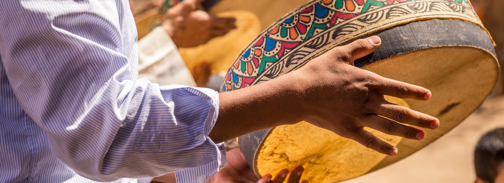 Man's hands holding round drum with ornate painted frame.