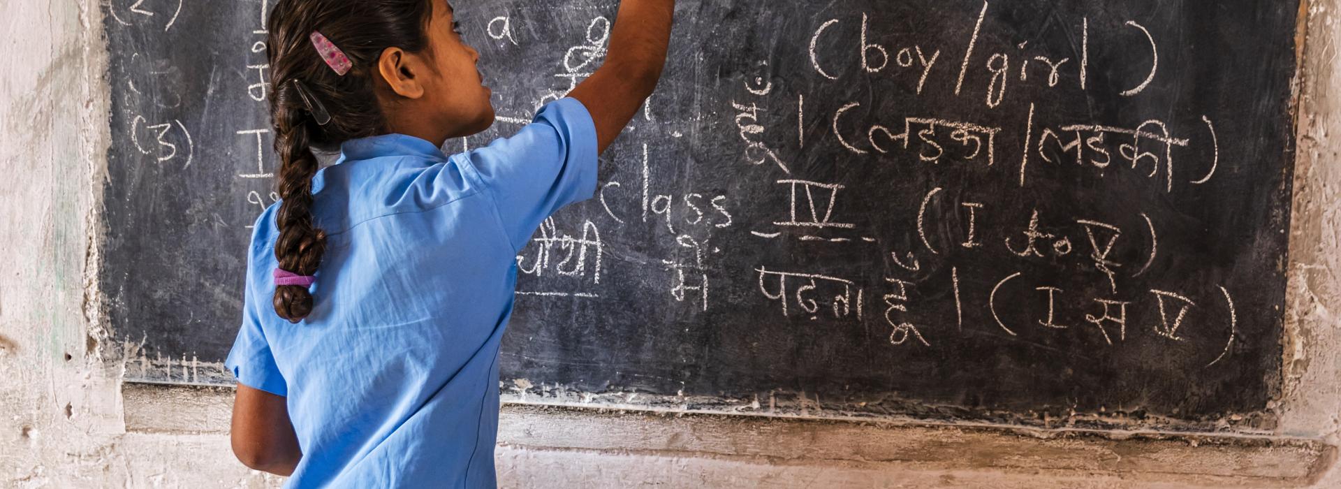 Young girl writing on chalkboard.