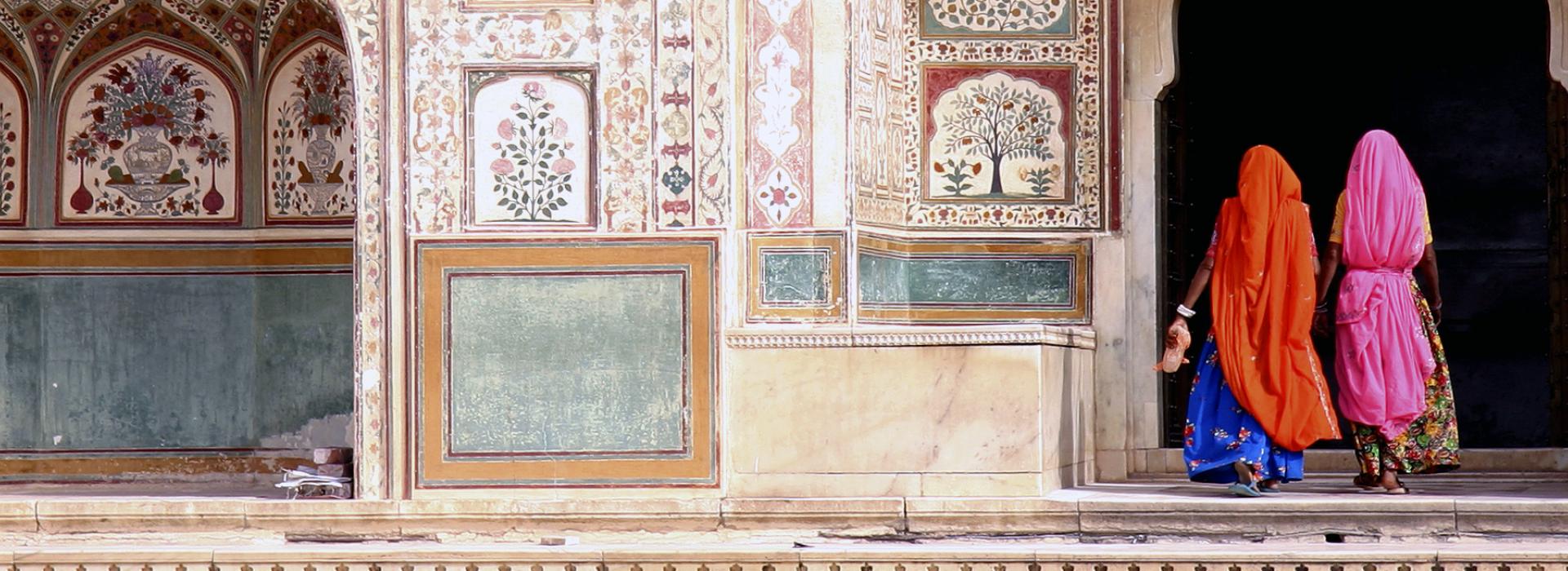 Women in traditional dress walking through ornate tiled doorway.